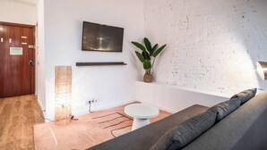 A modern living room with a flat-screen TV mounted on the wall, a potted plant, a round white table, and a grey sofa.