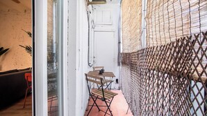 A narrow outdoor corridor with a wooden table and chairs, a white door, and a metal fence.