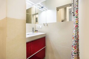 Casa de banho com lavatório branco, armário vermelho e cortina de chuveiro estampada com flores.