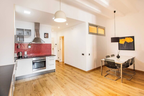 Cozinha moderna com painel de azulejos vermelhos, forno embutido e área de refeições com mesa e cadeiras.
