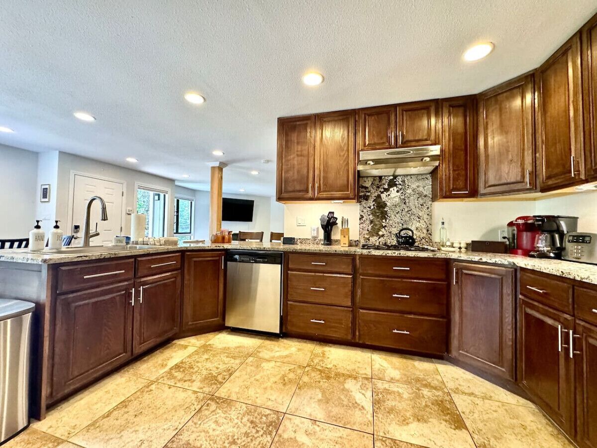 A modern kitchen with wooden cabinets, a dishwasher, granite countertops, and a built-in oven.