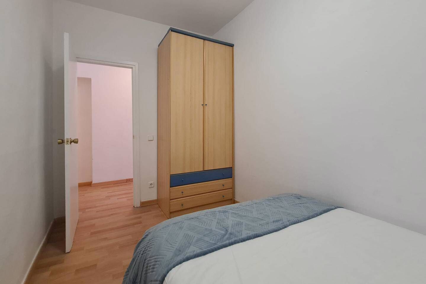A bedroom with a bed, a wardrobe, and a door leading to another room.