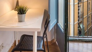 A balcony with a white table, a black chair, a potted plant, and a lamp. - 32ara1086 - 3 bedrooms apartment (Barcelona)
