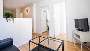 Ein modernes Wohnzimmer mit Glastisch, schwarzem Sofa, Flachbildfernseher und weißem Schreibtisch.