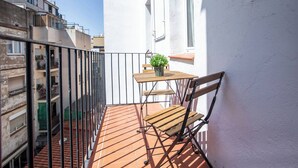 Ein kleiner Balkon mit Holztisch und Stuhl, einer Topfpflanze und Blick auf benachbarte Gebäude.
