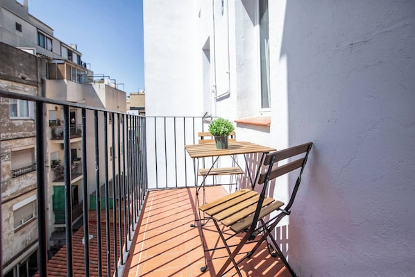 A small balcony with a wooden table and chair, a potted plant, and a view of neighboring buildings.