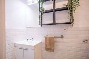Een badkamer met witte betegelde wanden, een witte wasbak, een handdoekhouder met een handdoek, en een spiegel met een zwarte lijst en planten.