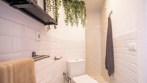 A small, white-tiled bathroom with a toilet, a towel rack, and a hanging plant. - BPAR1088 - Cozy flat near the beach (Barcelona)