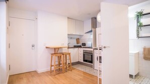 A compact kitchen with white cabinets, a wooden stool, a microwave, an oven, and a washing machine. - BPAR1088 - Cozy flat near the beach (Barcelona)