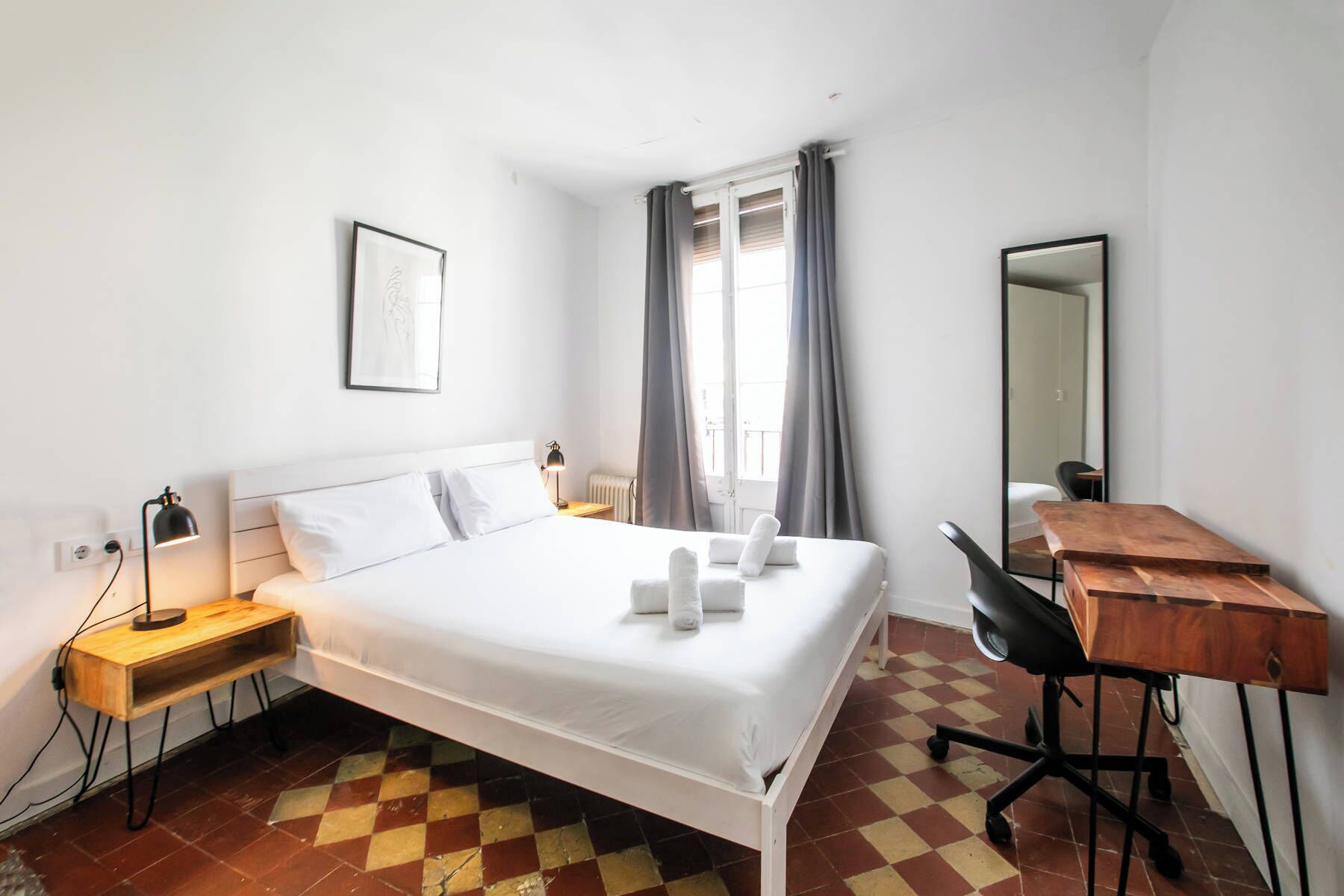 Une chambre d’hôtel comprenant un lit, une table de chevet, une lampe, un bureau, une chaise et un grand miroir.