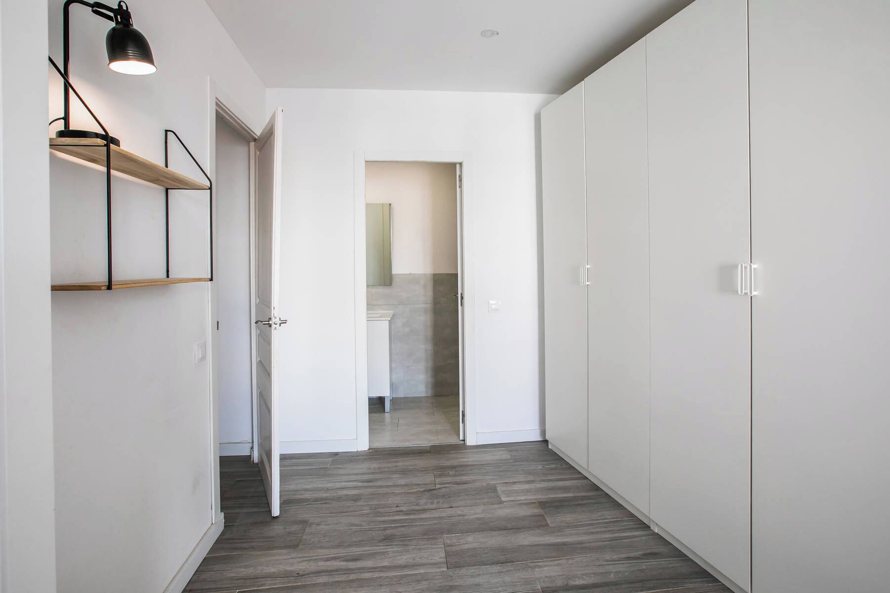 A hallway with a wooden floor, white walls, and a door leading to a bathroom.