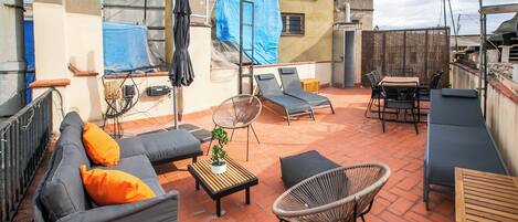 A rooftop terrace with a sofa, two lounge chairs, a small table, and a wicker chair.