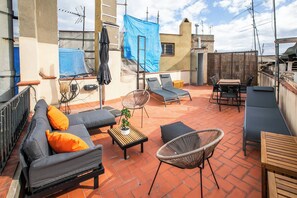 Une terrasse sur le toit aménagée avec un canapé, deux fauteuils, une petite table et une chaise en osier.