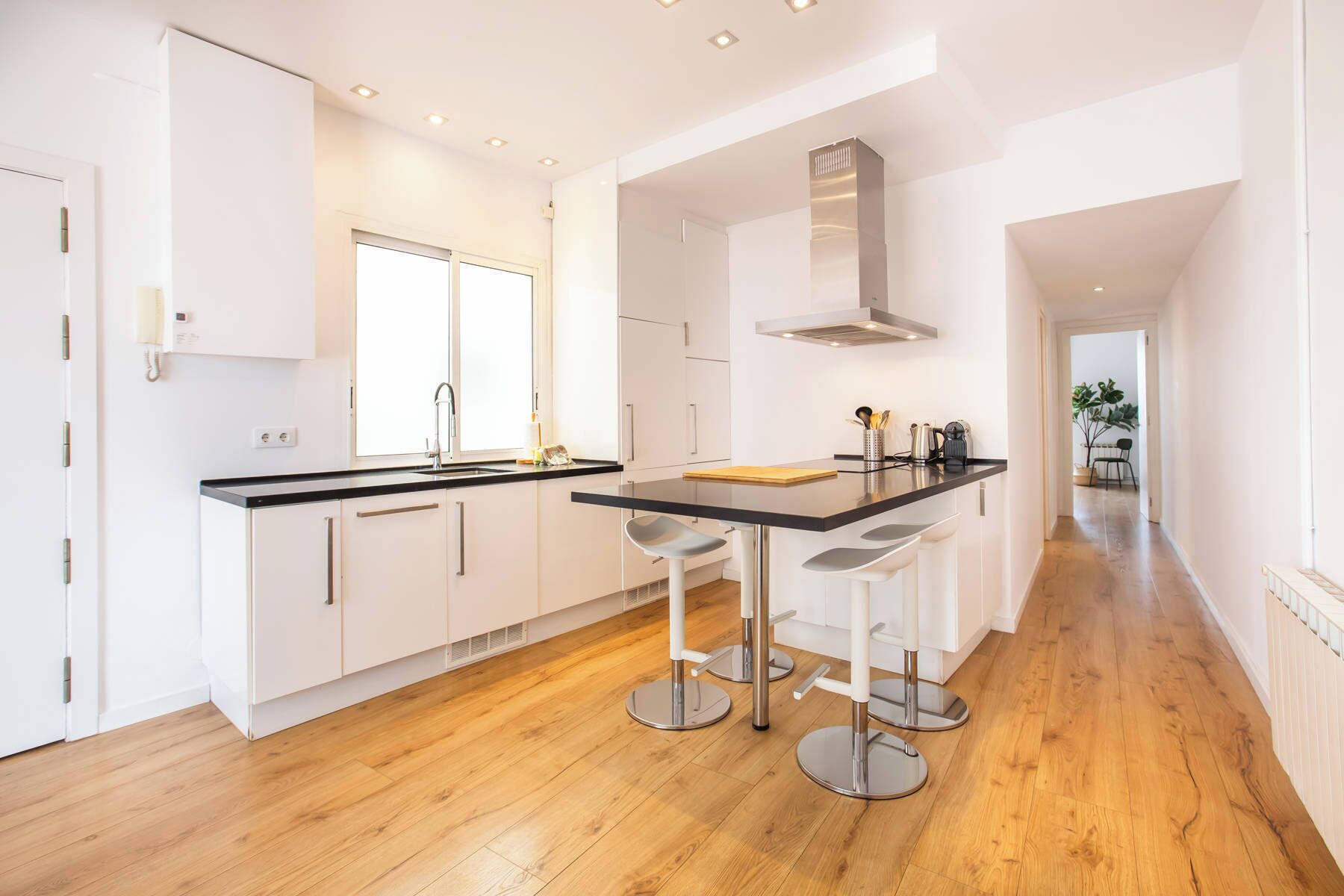 A modern kitchen with white cabinets, a black countertop, and stainless steel bar stools.