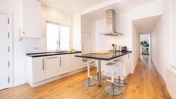 A modern kitchen with white cabinets, a black countertop, and stainless steel bar stools.