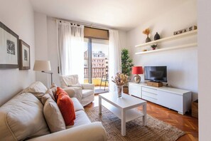 Un salon moderne comprenant un canapé, des fauteuils, une table basse, un téléviseur et un balcon offrant une vue sur la ville.