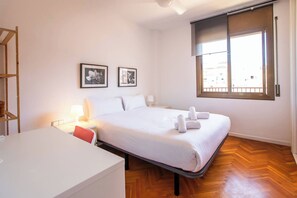 Une chambre d’hôtel avec un lit, un bureau, une chaise, une fenêtre et deux tableaux encadrés au mur.