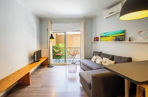 A compact living space with a sofa, a small table, a bench, and a balcony with a view.