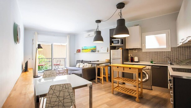 A compact kitchen with a dining area, a small seating space, and a view to an outdoor balcony.