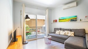 A modern living room with a grey sofa, a flat-screen TV, and a balcony with outdoor furniture.