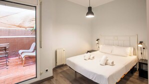 A modern bedroom with a large bed, two bedside lamps, a radiator, and a sliding glass door leading to an outdoor seating area.