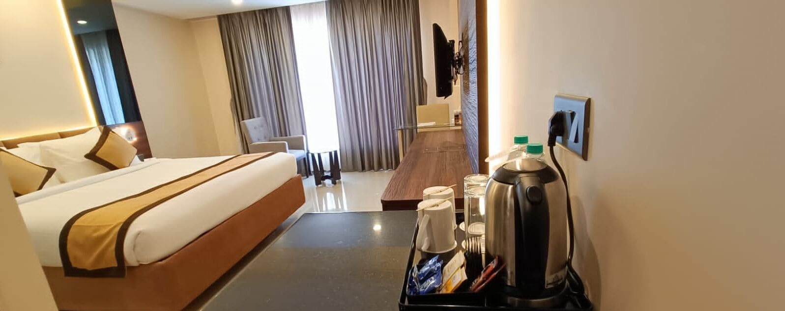 A hotel room with a bed, a coffee maker, and a TV on the wall.