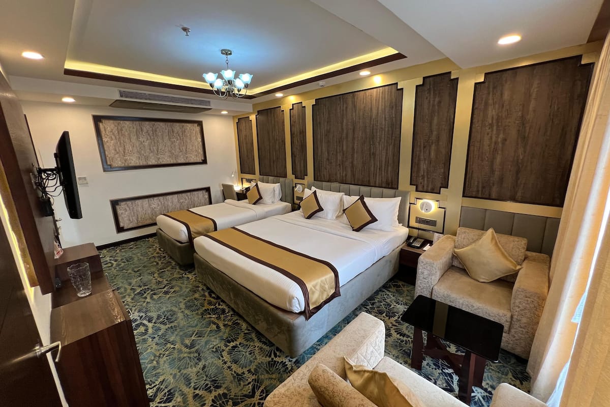 A hotel room with a large bed, two bedside tables, a TV, and a seating area with a sofa and armchairs.