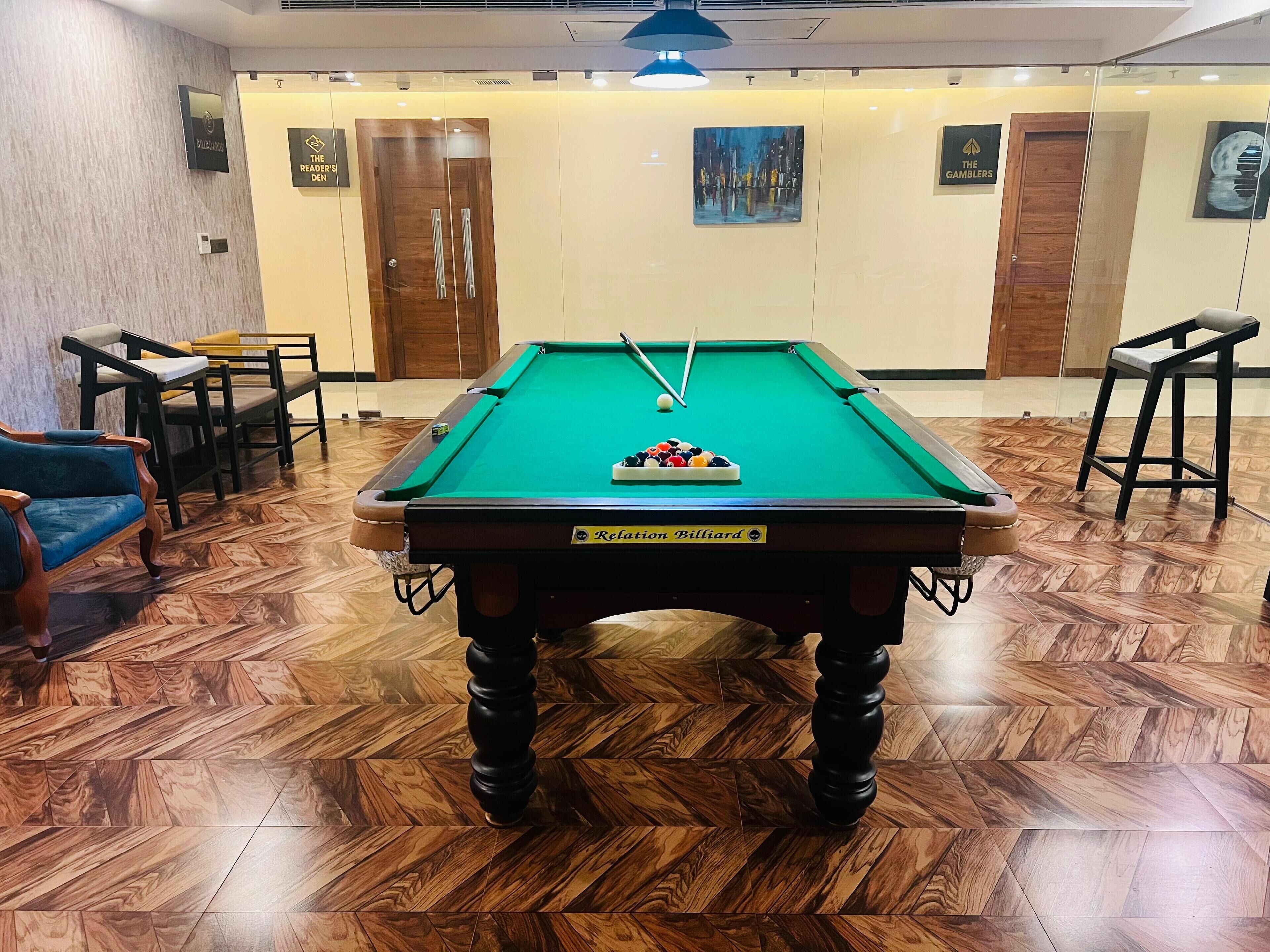 A billiards table labeled "Relaction Billiard" in a room with wooden parquet flooring, two doors, and a painting on the wall.