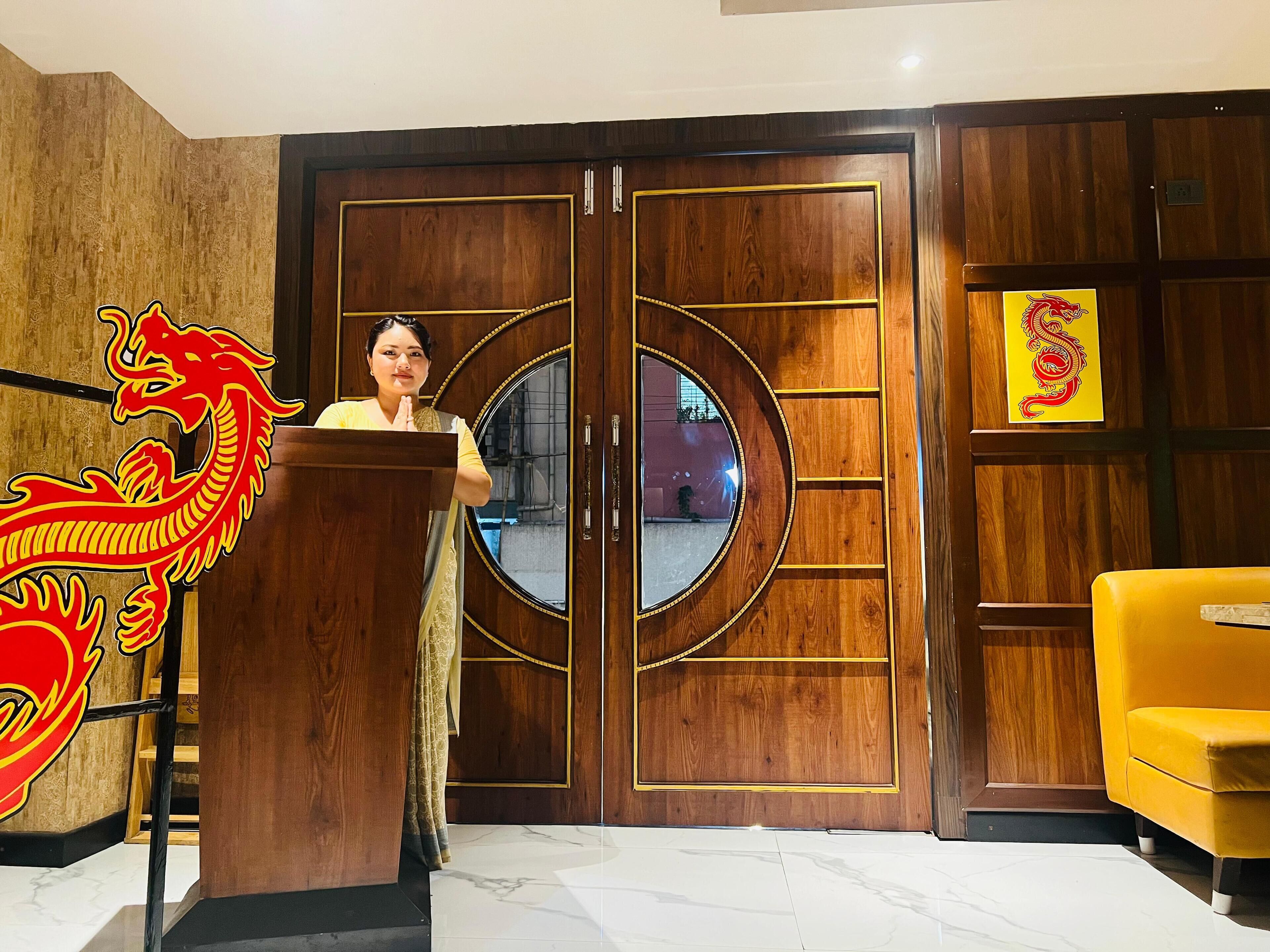 A person standing at a wooden podium with a dragon design, in front of a large wooden door with a circular mirror.