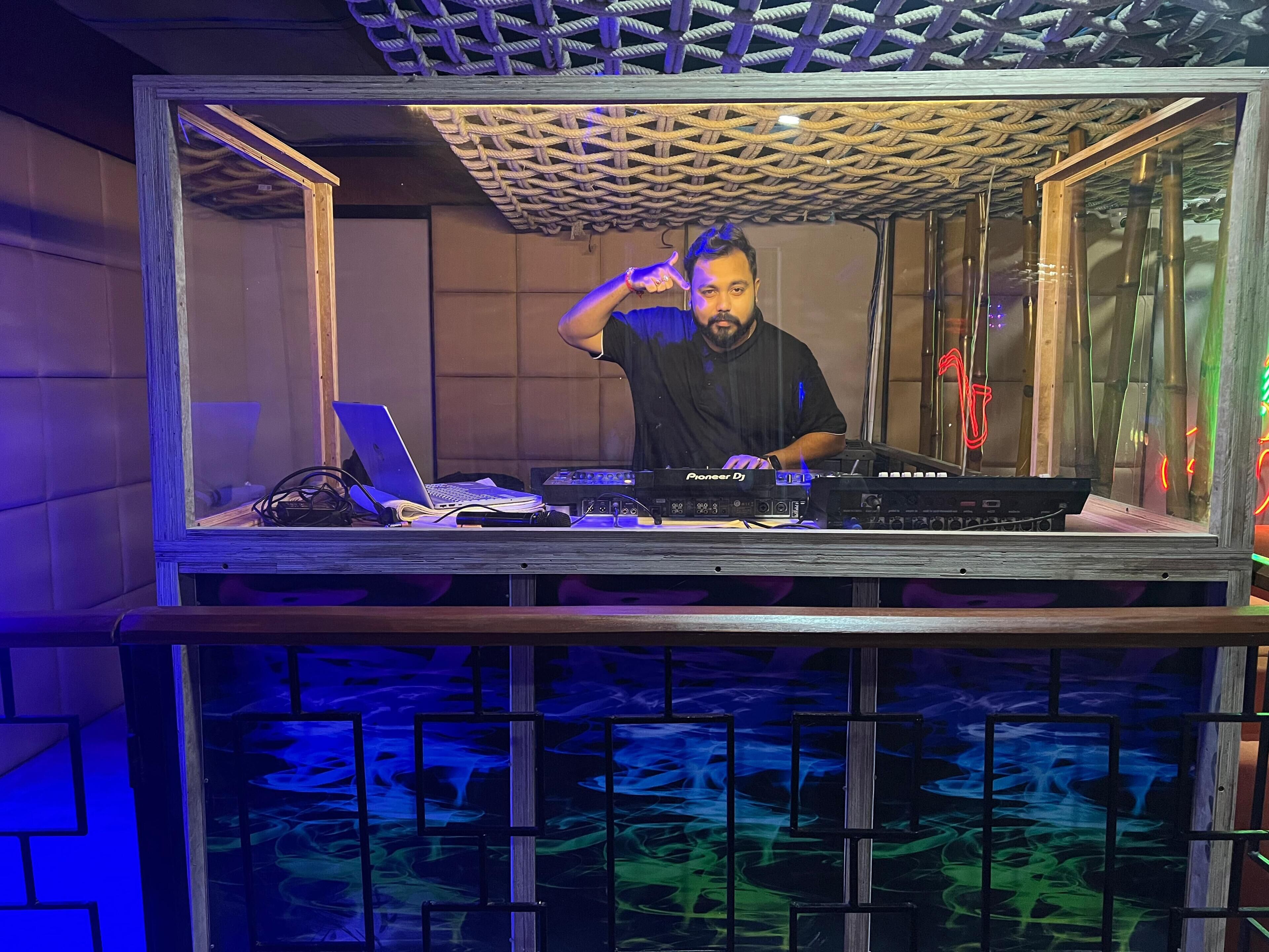 A DJ booth with a laptop, Pioneer DJ controller, and a wooden structure with a woven ceiling.