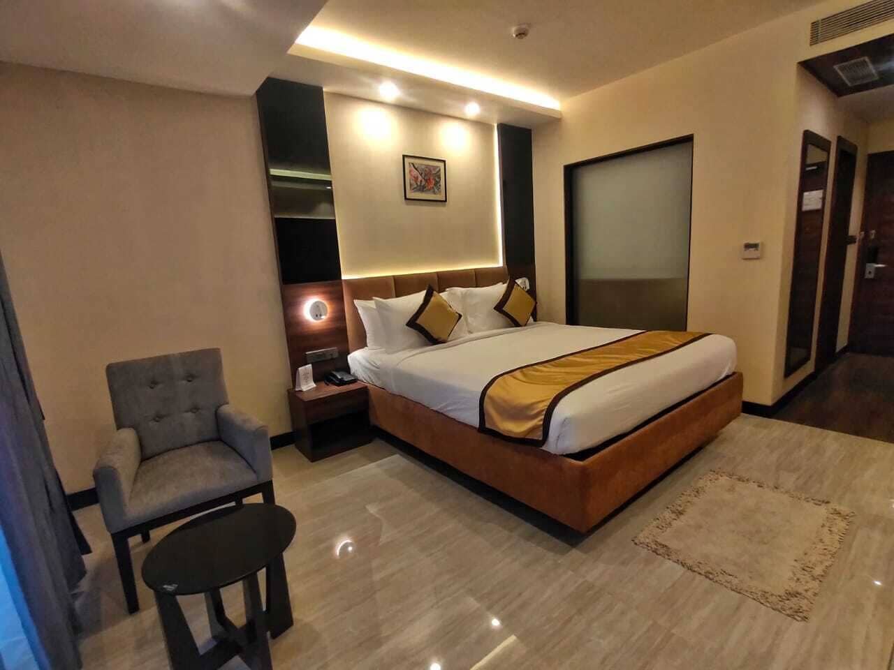 Habitación de hotel con cama, una silla, mesita de noche y un cuadro colgado en la pared.