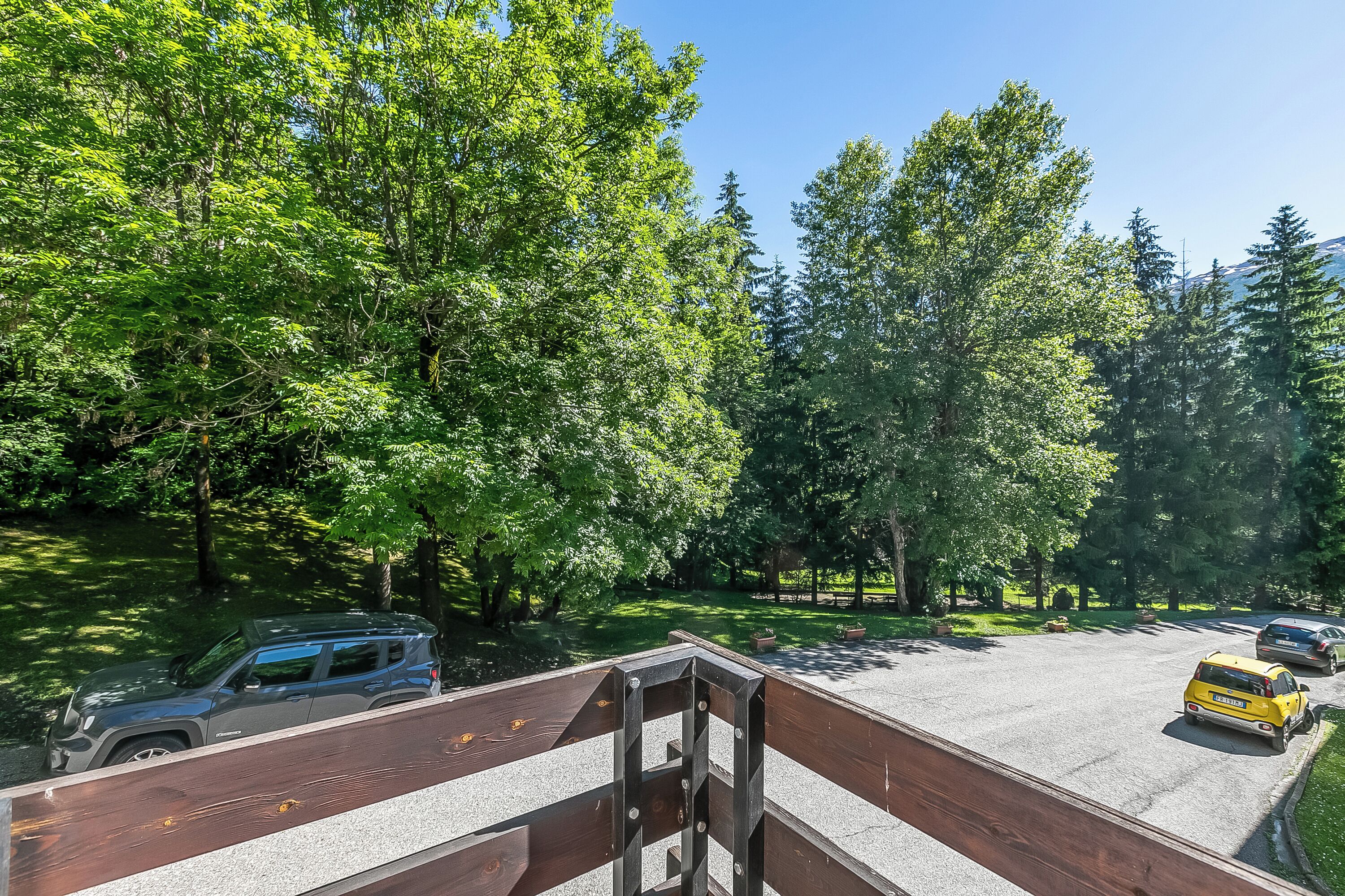 A parking area with vehicles, surrounded by trees and a clear sky.