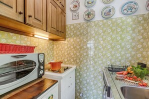 A kitchen with a toaster oven, a stove, and a sink. There are plates with designs on the wall and a basket on the counter. - Alme Suites Near Slopes of Campo Smith (Bardonecchia)
