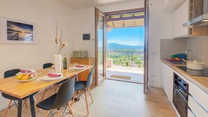 A modern kitchen with a view to the outdoors, a dining area with a table set for two, and a balcony with a scenic view. - Il Vecchio Faggio: Lake Maggiore View Terrace (Gignese)