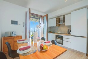 Une cuisine moderne avec des meubles blancs, une table à manger en bois mise avec des assiettes, des verres et un panier de fruits.