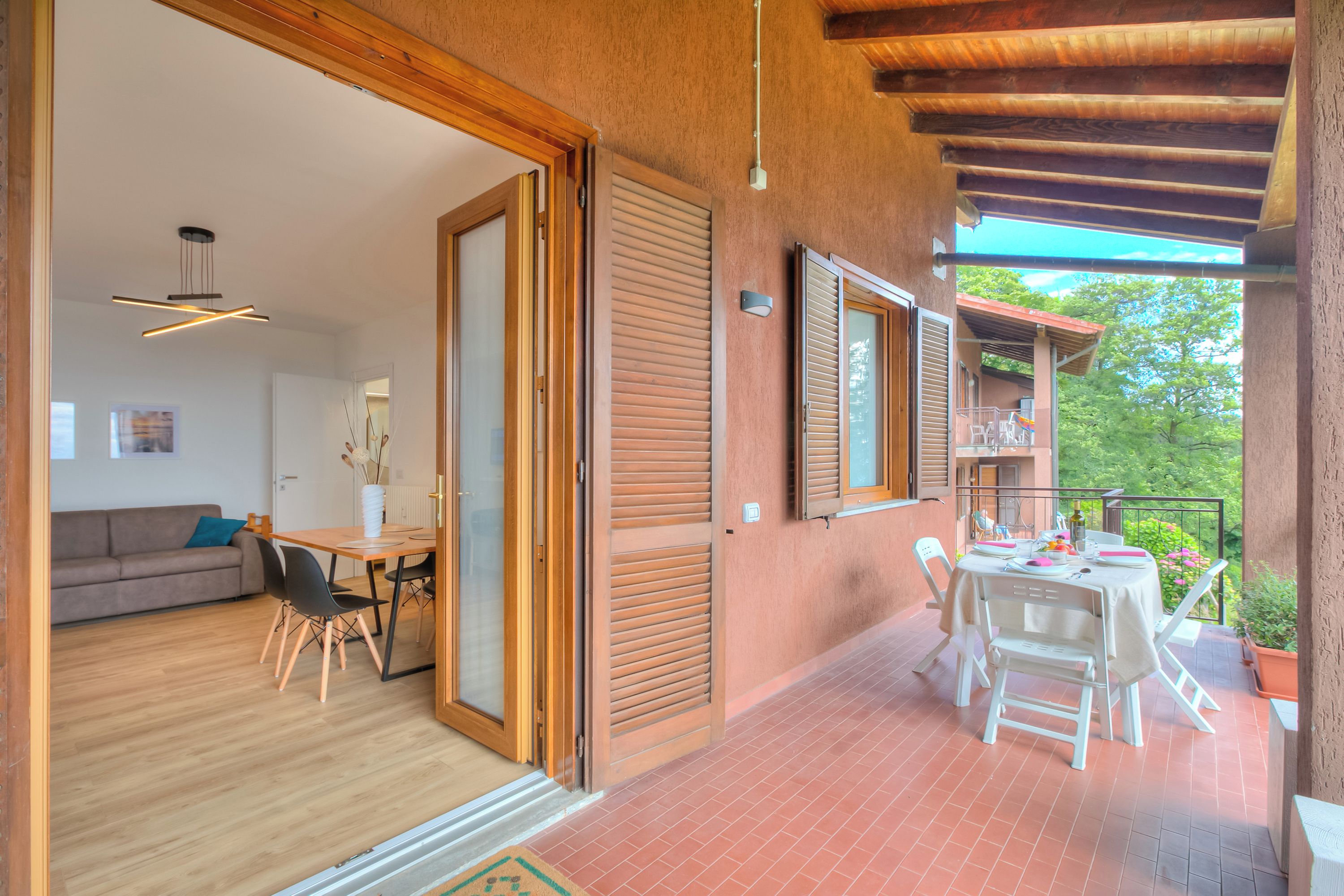 Un salón amplio con techo de madera, una mesa de comedor con sillas, un sofá y un balcón con vistas a zonas verdes.