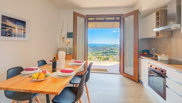 A modern kitchen with a view, a dining area with a table set for two, and a large window. - Il Vecchio Faggio: Lake Maggiore View Terrace (Gignese)