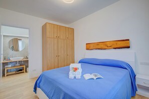 Camera da letto con un letto, un'armadiatura in legno, uno specchio e un bagno con lavandino e mobiletti.