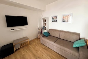 A living room with a flat-screen TV, a sofa, a bench, a bookshelf, and two framed pictures on the wall. - Il Vecchio Faggio (Gignese)