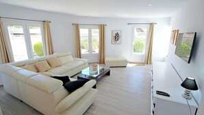 Un salon moderne avec un canapé d’angle, une table basse en verre et un meuble TV blanc.