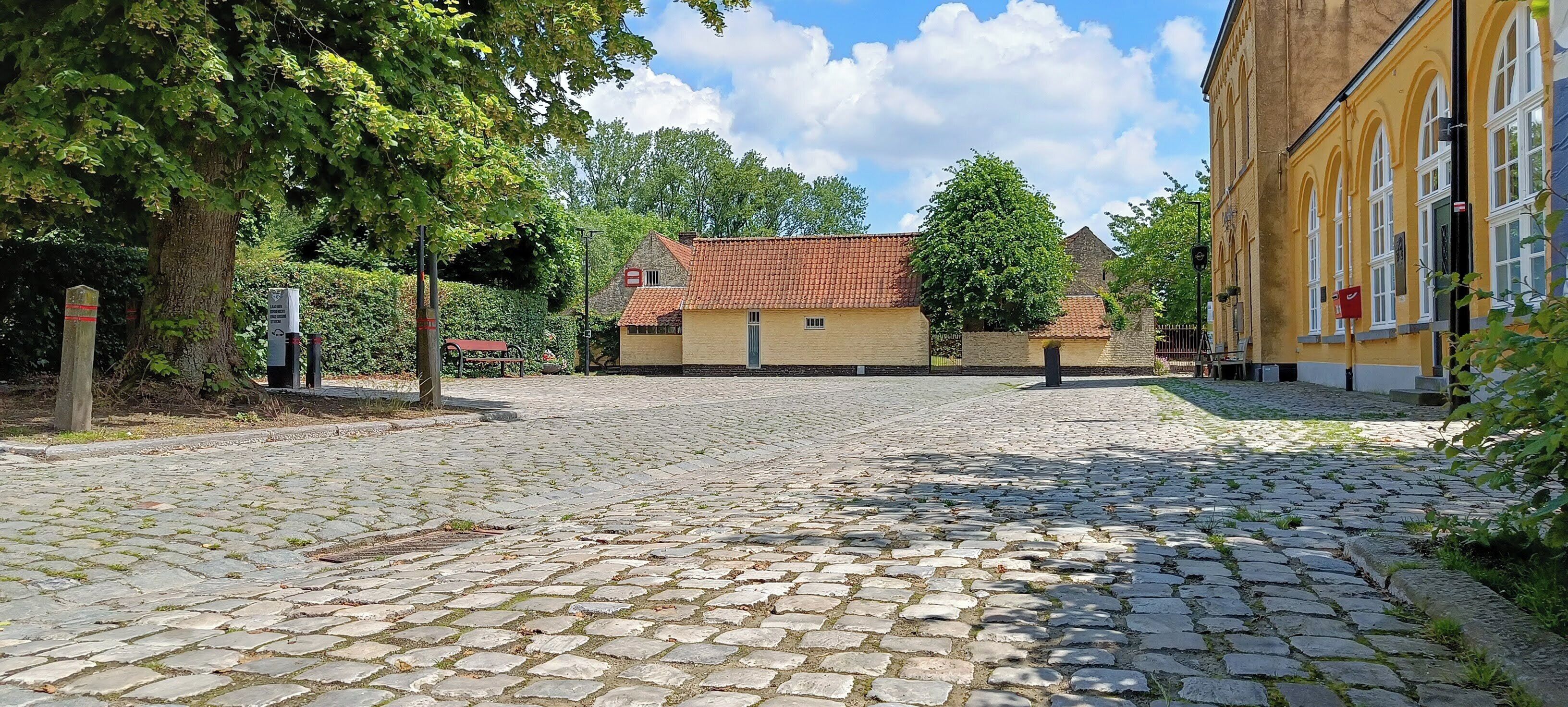 A cobblestone courtyard with a building featuring a red-tiled roof and a yellow facade.
