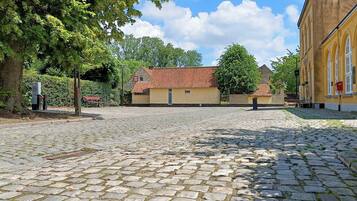 A cobblestone courtyard with a building featuring a red-tiled roof and a yellow facade.