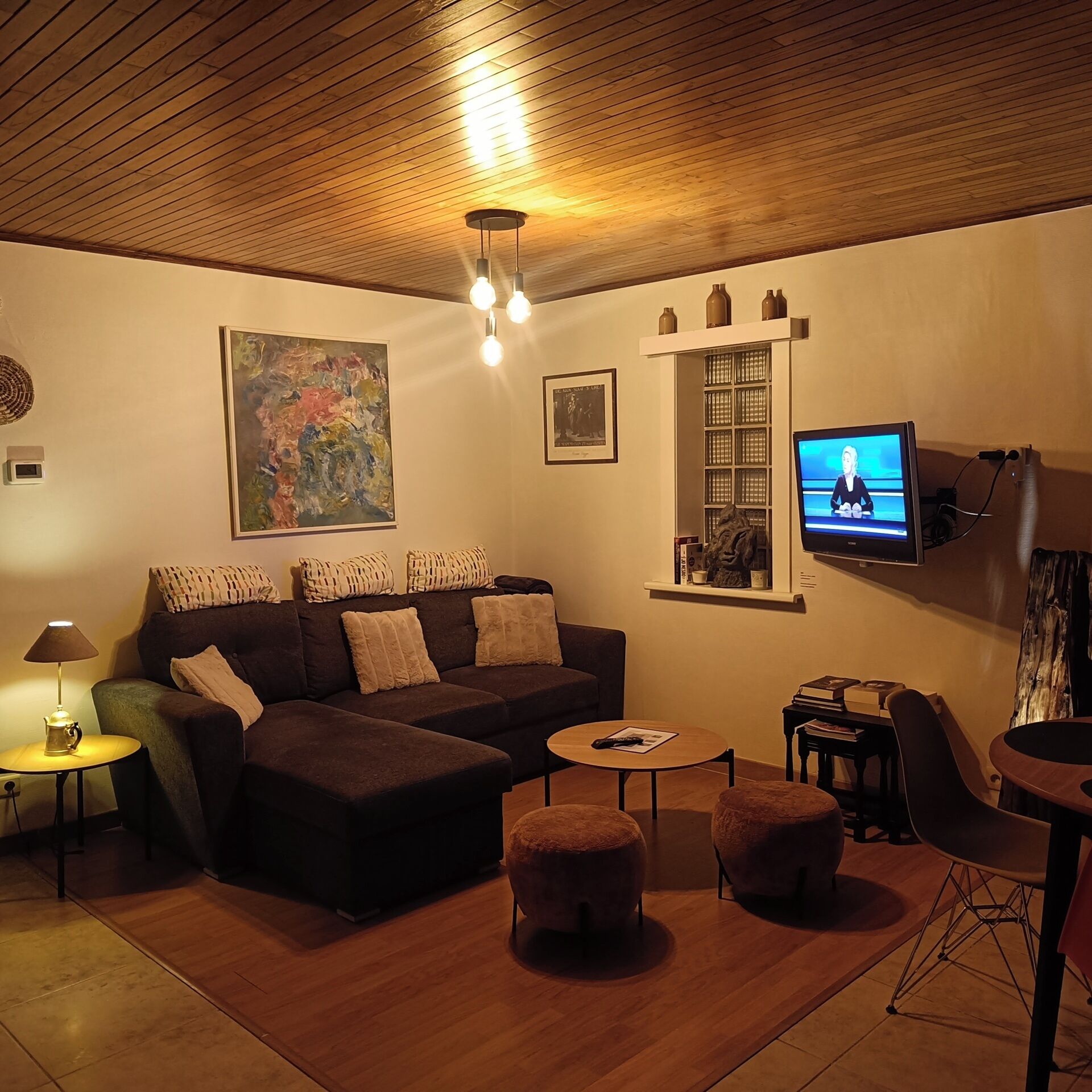 A cozy living room with a dark brown sofa, a small round table, and a television mounted on the wall.