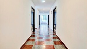 A long, narrow hallway with a checkered floor pattern and doors on both sides. - iROOMZ Elite Casa Grand Inn (Hyderabad)