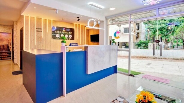 A hotel reception area with a modern design, featuring a reception desk, a digital clock, and a sign for 'Casa Grand Inn'. - iROOMZ Elite Casa Grand Inn (Hyderabad)