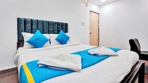 A neatly made bed with blue and white bedding, a dark headboard, and a wooden door in the background. - iROOMZ Elite Casa Grand Inn (Hyderabad)
