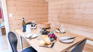 Une table de salle à manger en bois, mise avec des assiettes, des couverts, des verres, un pichet, une bouteille et une planche à fromage garnie de raisins.