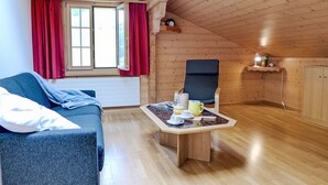 Une pièce chaleureuse avec un plafond en bois, un canapé bleu, une table en bois avec une lampe et une chaise.
