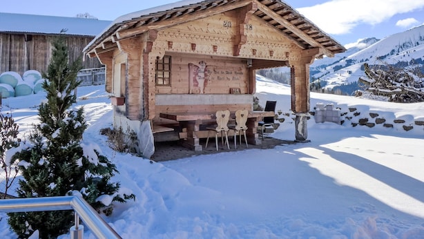 Un chalet en bois avec un toit en pente, un banc à l’extérieur et une vue sur des montagnes enneigées.
