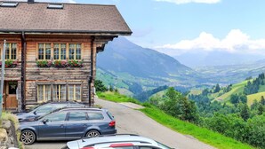 Une maison en bois avec un toit en pente et des jardinières aux fenêtres. Des voitures sont garées devant.